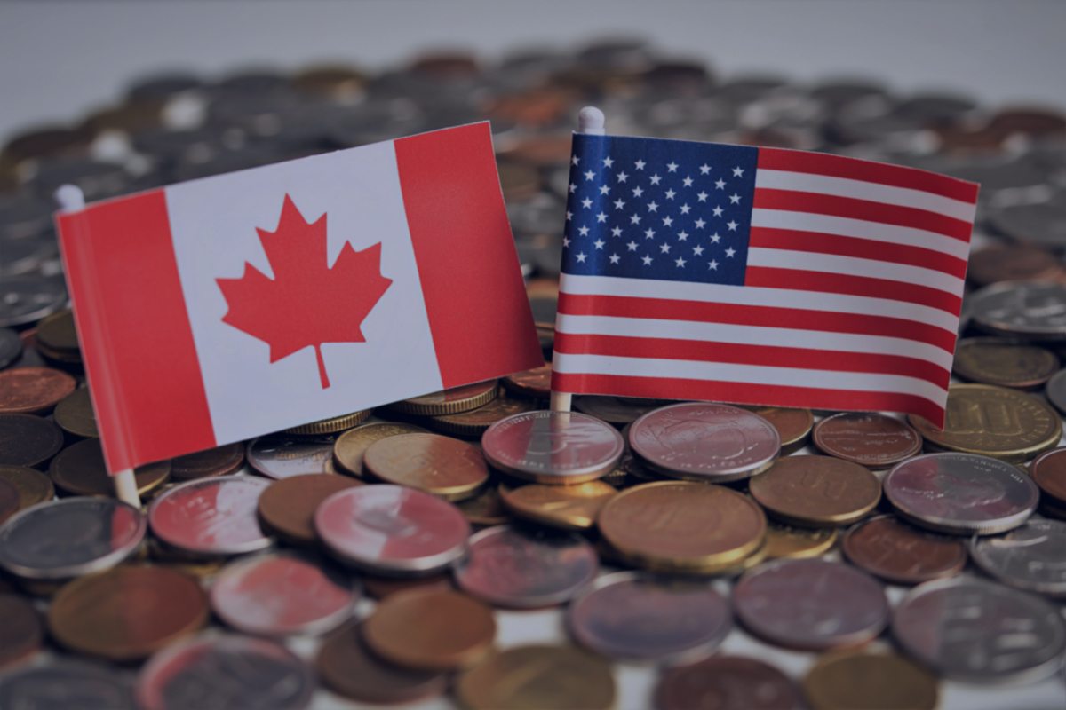 Two small flags, one Canadian and one American, stand upright in a pile of mixed coins